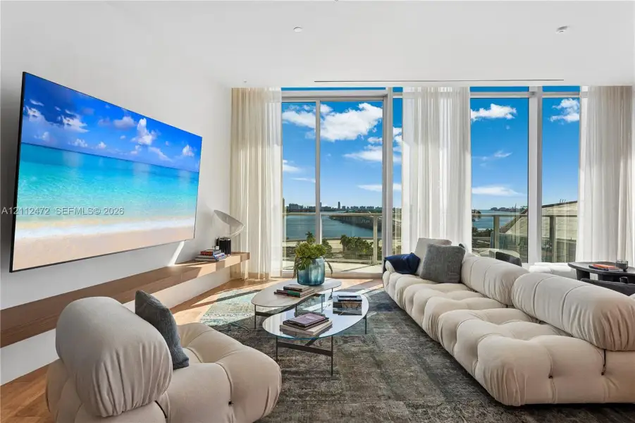 Floor-to-ceiling windows, wood-finish flooring, and a wall-mounted floating wood shelf