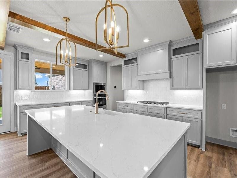 Kitchen featuring gray cabinets, beamed ceiling, light stone countertops, a spacious island, and a breakfast bar Kitchen featuring gray cabinets, beamed ceiling, light stone countertops, a spacious island, and a breakfast bar