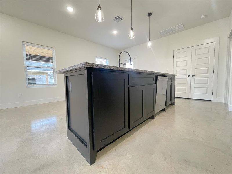 Kitchen featuring light stone countertops, sink, a kitchen island with sink, hanging light fixtures, and dishwashing machine