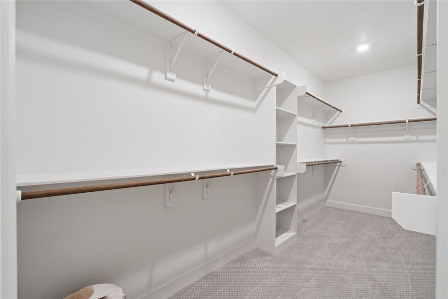 Expansive walk in closet with multiple hanging sections and built in shelving for structured organization.