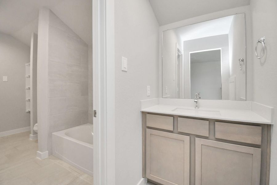 Experience convenience in the secondary bathroom, designed for Jack and Jill arrangements, now with a separate vanity area. This well-appointed space showcases stylish tile flooring, a bath/shower combo with an elegant tile surround, and light-stained wood cabinets. The beautiful light countertop adds a touch of sophistication, combining functionality and aesthetics seamlessly. Sample photo of completed home with similar floor plan. Actual colors and selections may vary.