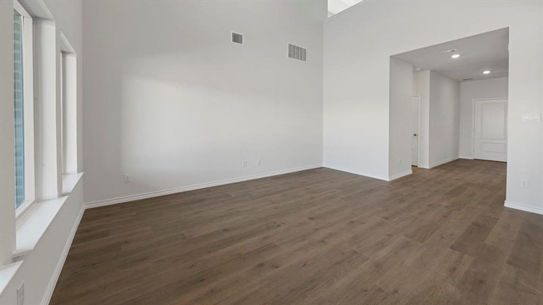 Spacious room featuring wood-finish flooring, white baseboards, and bright white walls Spacious room featuring wood-finish flooring, white baseboards, and bright white walls
