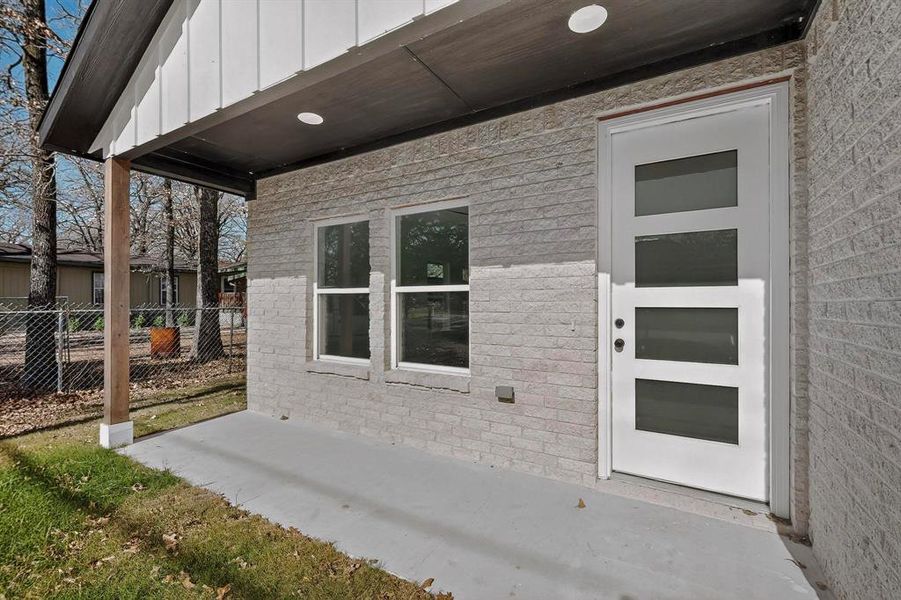 View of exterior entry with a patio area, board and batten siding, and brick siding