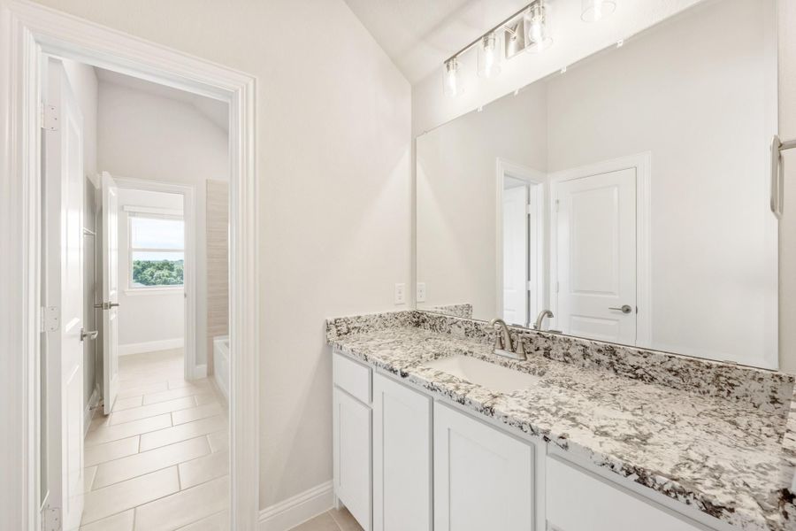 Bathroom with white cabinets, granite countertop, large mirror, and view into tiled shower area