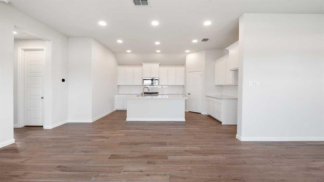 Kitchen featuring white cabinets, backsplash, a kitchen island with sink, hardwood / wood-style flooring, and sink