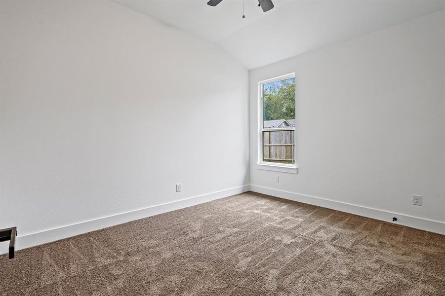 Carpeted empty room featuring ceiling fan and vaulted ceiling