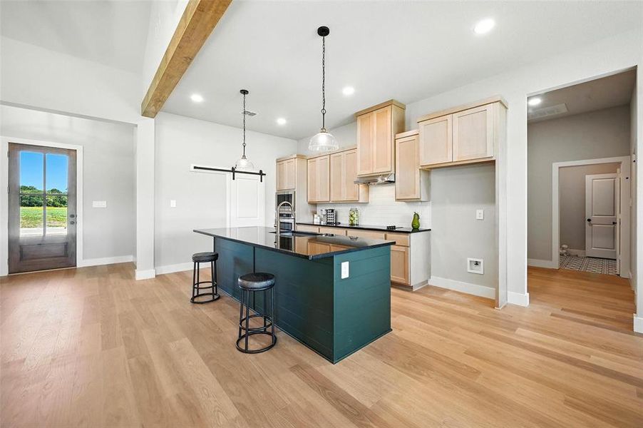 Kitchen featuring light wood finish cabinets, a kitchen island with sink, light wood-type flooring, a breakfast bar, and a barn door