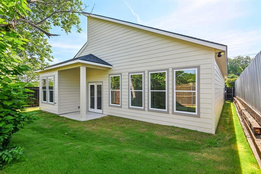 Rear exterior featuring horizontal siding, a covered patio with a double-door entry, a series of three large windows, and a manicured lawn