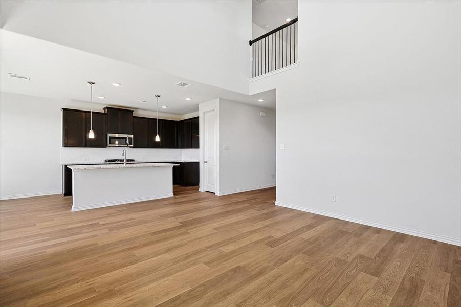 Kitchen featuring light hardwood / wood-style flooring, decorative light fixtures, dark brown cabinets, and a kitchen island with sink