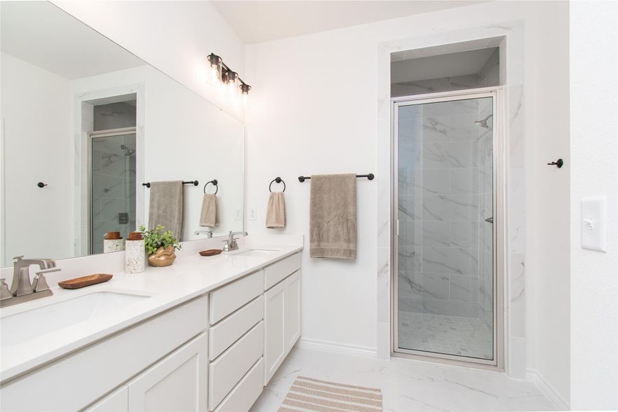 Bathroom featuring a marble finish shower, double vanity, and light marble finish floors
