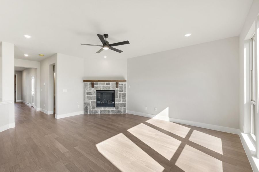 Open living room with stone fireplace, wood mantel, hardwood floors, and ceiling fan