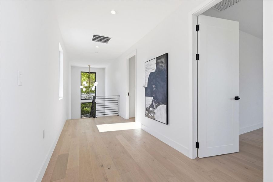 Hallway with light wood finished floors, an upstairs landing, and a chandelier