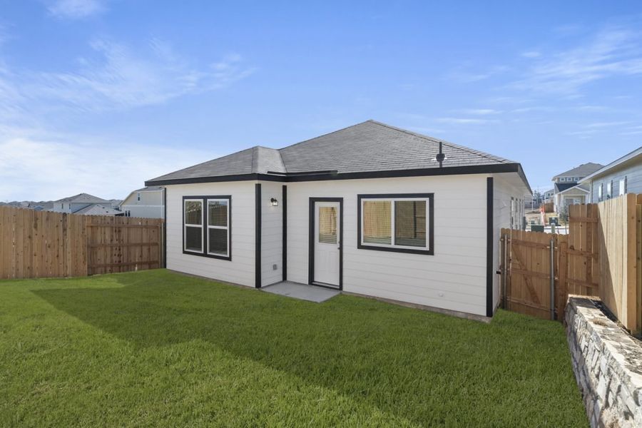 Image of a white one story house back exterior with black trim, a green grass backyard, a wooden fence and a blue sky in the background Image of a white one story house back exterior with black trim, a green grass backyard, a wooden fence and a blue sky in the background