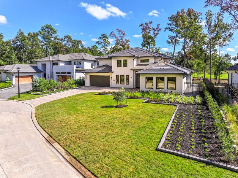 This modern two-story home features a sleek design with large windows and a spacious driveway. It has a well-maintained front lawn and landscaped garden beds, offering a welcoming curb appeal. Surrounded by trees, the property provides a sense of privacy and natural beauty.