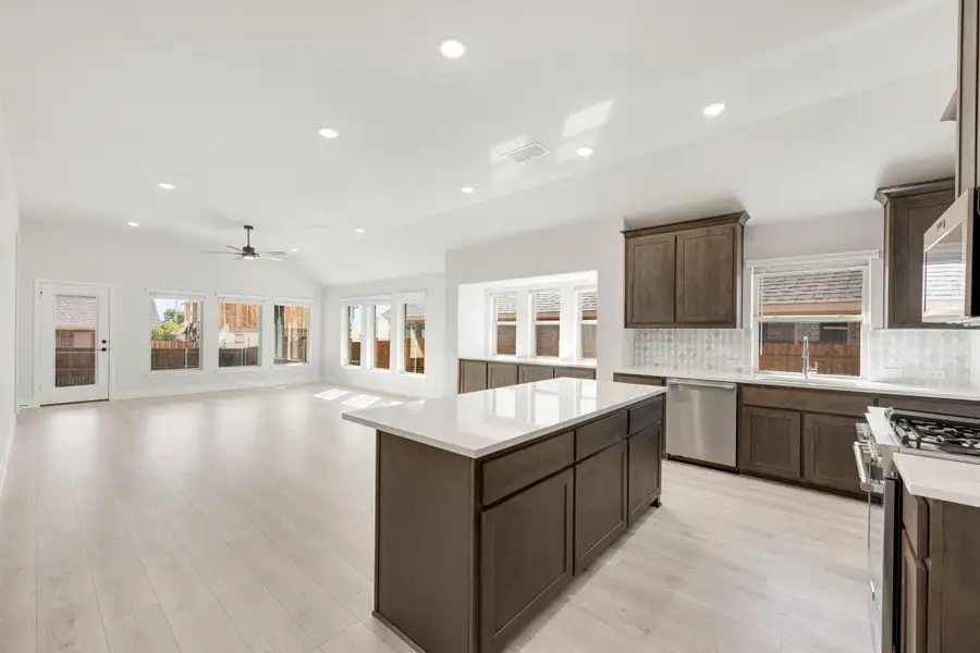 Open kitchen with dark wood cabinets, center island, white countertops, and light hardwood floors open to living area