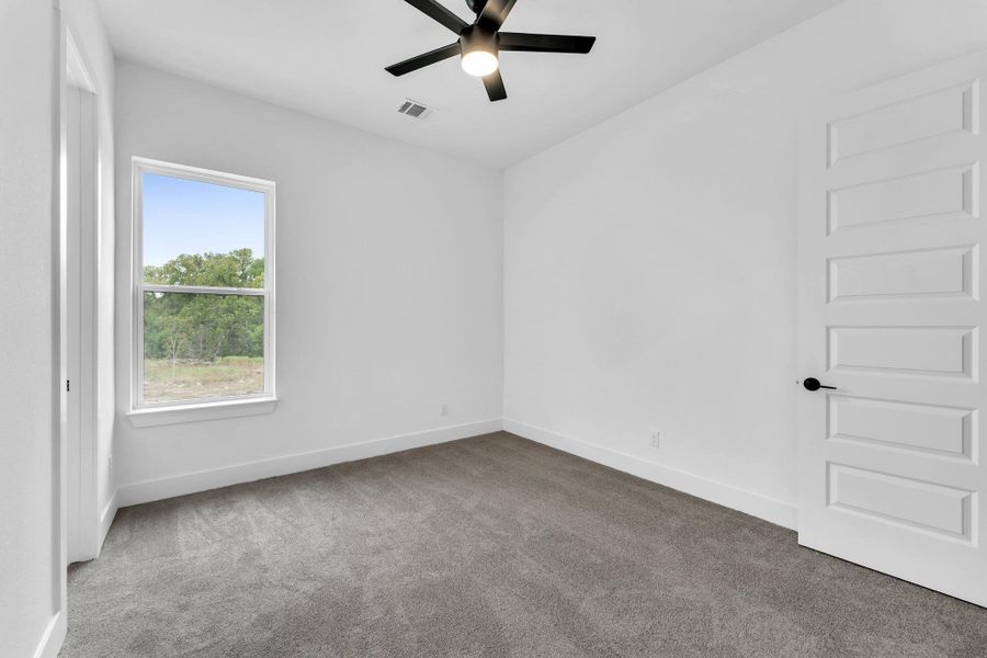 A well-lit bedroom features plush carpeting and a modern ceiling fan, offering tranquil views of the natural landscape. A well-lit bedroom features plush carpeting and a modern ceiling fan, offering tranquil views of the natural landscape.
