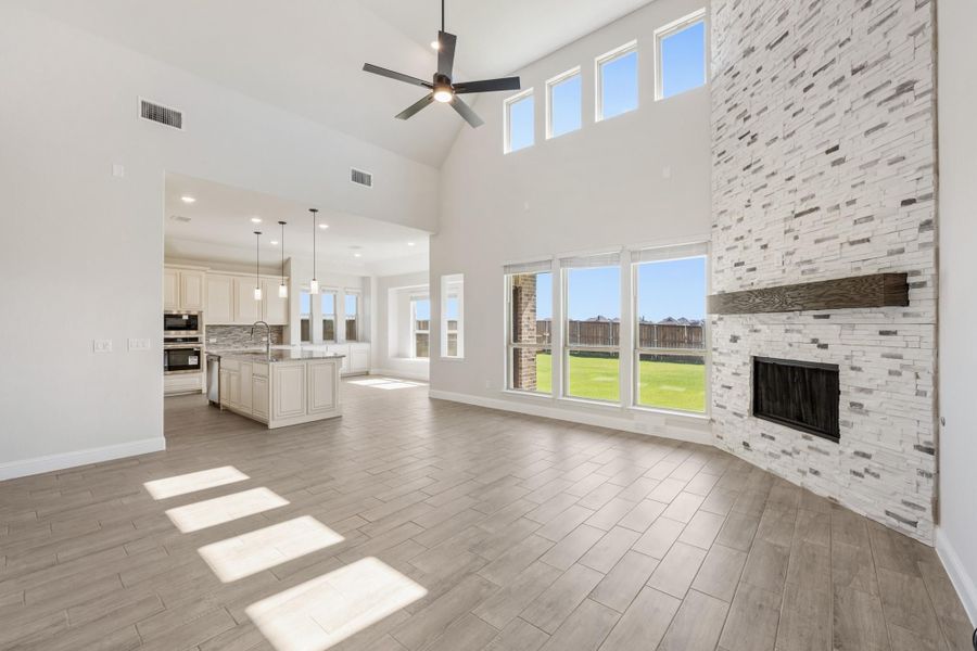 Open living room with vaulted ceiling, stone fireplace, and open kitchen with island visible in background Open living room with vaulted ceiling, stone fireplace, and open kitchen with island visible in background