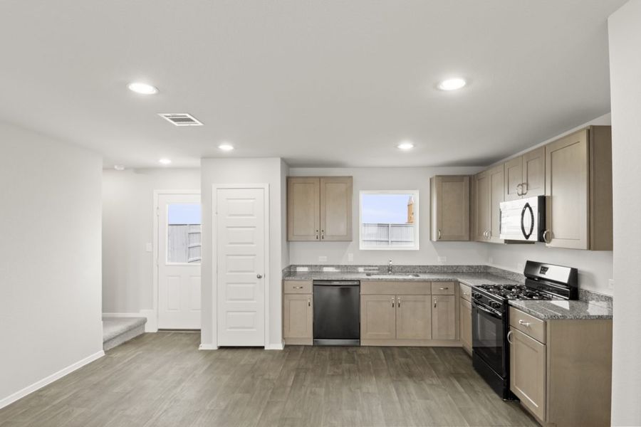Image of a kitchen with granite countertops, black appliances, and light brown cabinetry