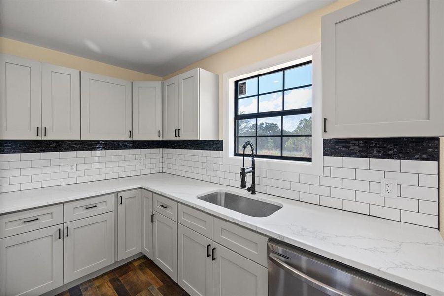 Kitchen with stainless steel dishwasher, tasteful backsplash, sink, light stone countertops, and dark hardwood / wood-style floors