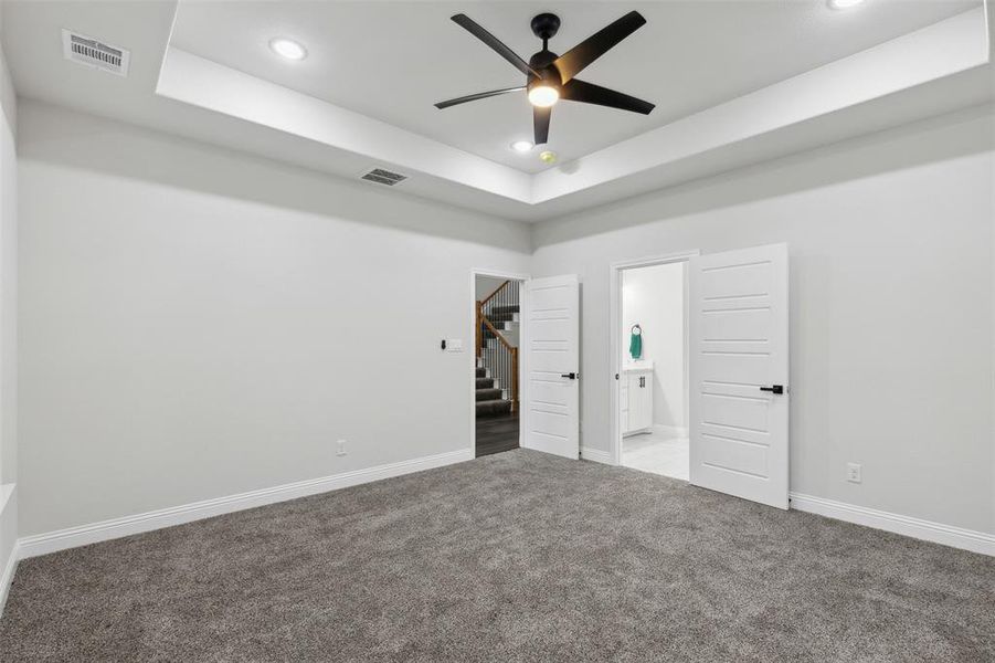 Unfurnished bedroom featuring ceiling fan, light colored carpet, a raised ceiling, and ensuite bath