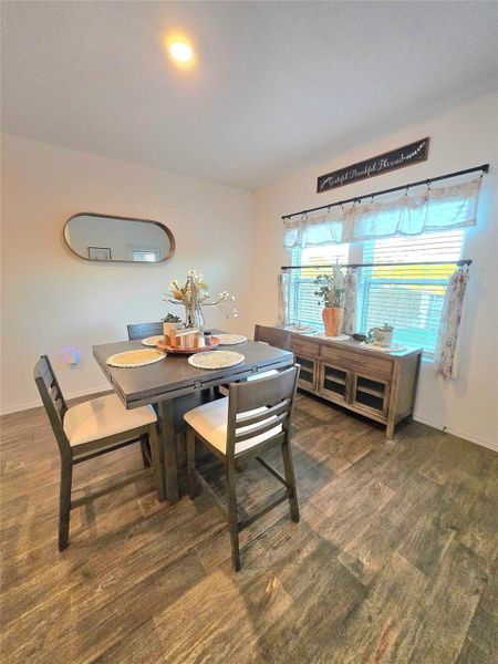 Dining area featuring wood-finish flooring, a wall-mounted mirror, and natural light from a window with blinds