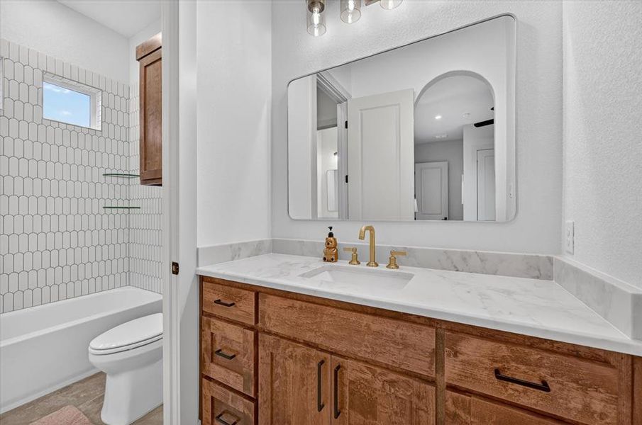 Bathroom featuring a wood-finish vanity with a single basin, a light-toned countertop, and a contemporary wall-mounted mirror