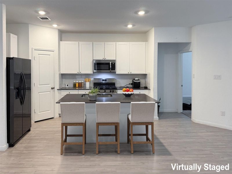 A contemporary kitchen features bright white cabinetry, dark countertops, and modern stainless steel appliances.