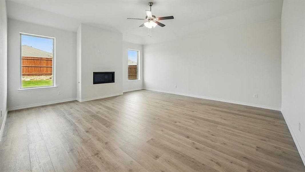 Unfurnished living room featuring a glass covered fireplace, light wood-style floors, plenty of natural light, and a ceiling fan