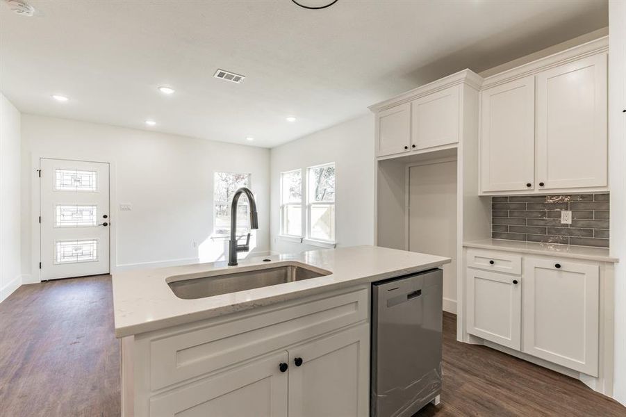 Kitchen featuring tasteful backsplash, dishwasher, sink, white cabinets, and light stone countertops