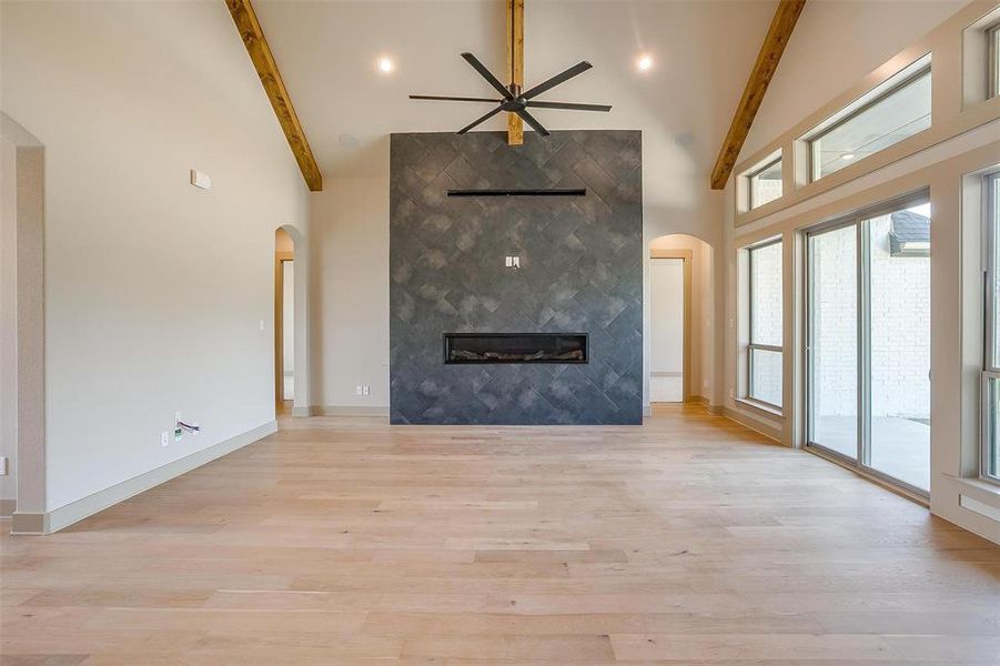 Unfurnished living room featuring beamed ceiling, arched walkways, and high vaulted ceiling