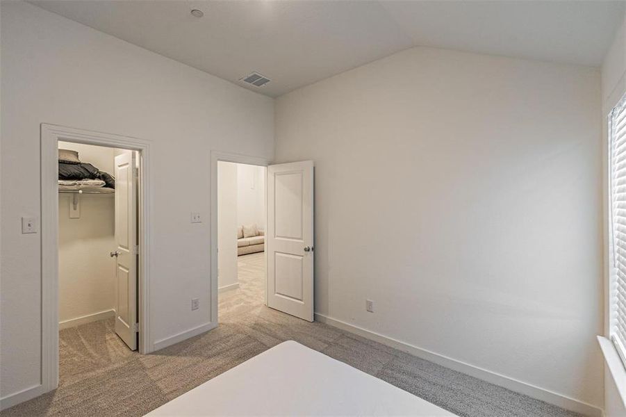 Unfurnished bedroom with light colored carpet, a walk in closet, and lofted ceiling