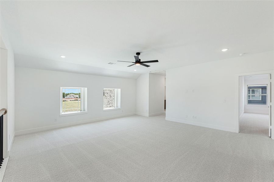 Large open bonus room with light carpet, black ceiling fan, and two windows