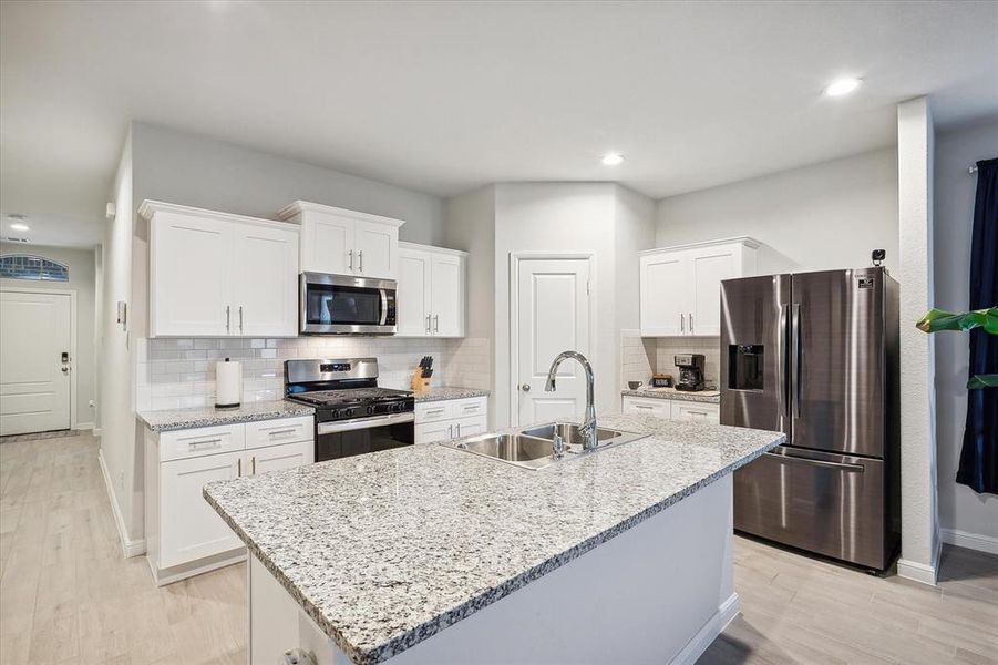 Kitchen with an island with sink, stainless steel appliances, backsplash, sink, and white cabinets Kitchen with an island with sink, stainless steel appliances, backsplash, sink, and white cabinets