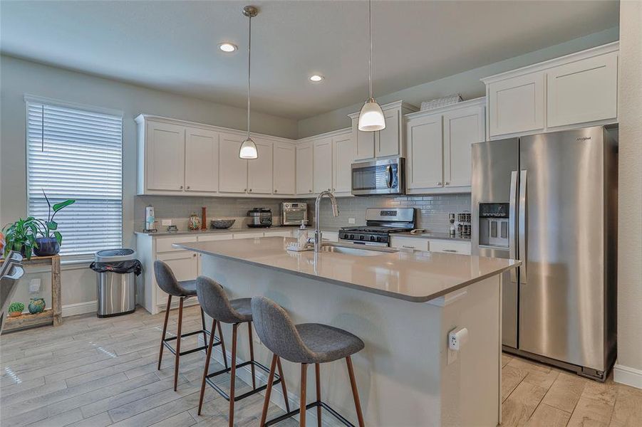 Kitchen featuring appliances with stainless steel finishes, backsplash, white cabinets, a center island with sink, and recessed lighting Kitchen featuring appliances with stainless steel finishes, backsplash, white cabinets, a center island with sink, and recessed lighting