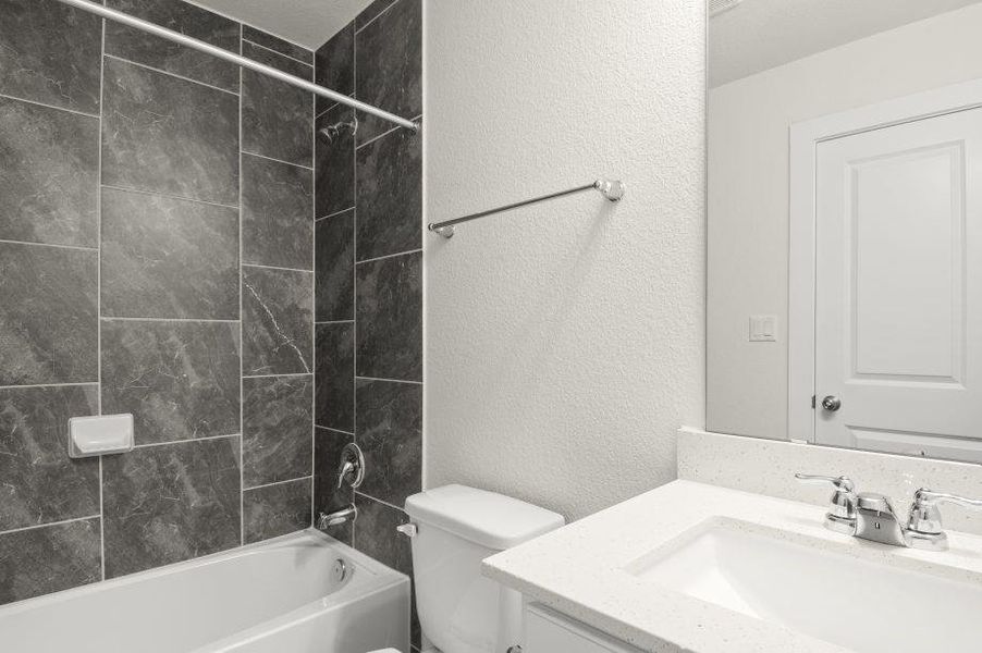 A well-appointed bathroom offers sleek tiled shower walls, a pristine tub, and a vanity with a generous countertop.