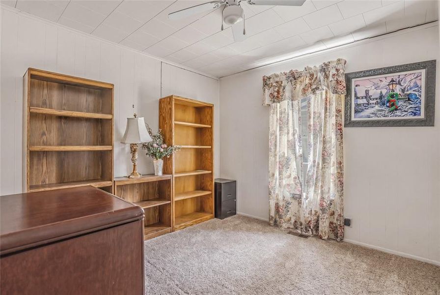 Carpeted room featuring white paneling, a drop ceiling, and a window with floral drapes Carpeted room featuring white paneling, a drop ceiling, and a window with floral drapes