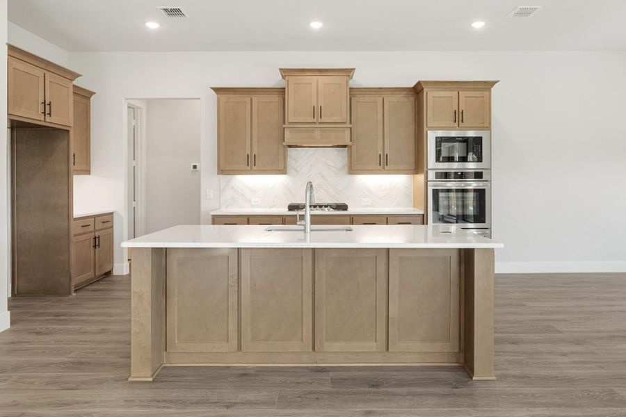 Kitchen with large center island, light wood cabinets, white countertops, and stainless steel double oven