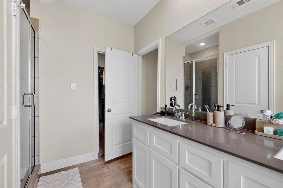 Full bathroom featuring a shower stall, vanity, a walk in closet, and light wood-style floors Full bathroom featuring a shower stall, vanity, a walk in closet, and light wood-style floors