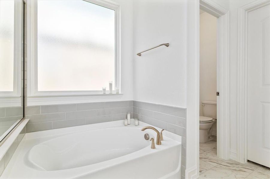 Soaking tub featuring a bronze-finish faucet, subway tile surround, and frosted window