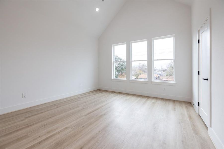 This thoughtfully designed primary bedroom features durable wood-like LVP flooring throughout. Cathedral ceilings are anchored by a stylish black ceiling fan, while three oversized windows, paired with recessed lighting, illuminate the space.