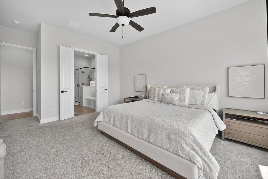 Spacious bedroom featuring light grey carpeting, light grey walls, and a dark-bladed ceiling fan