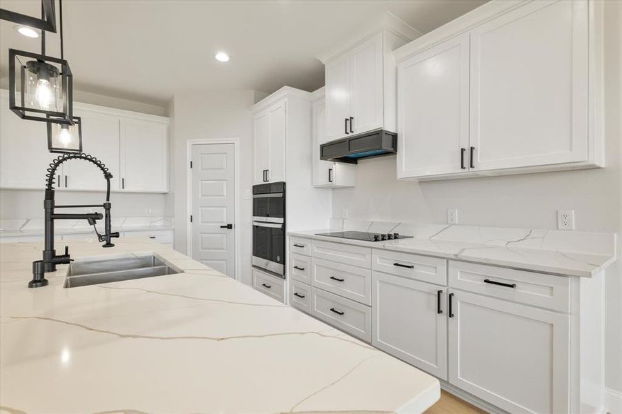 Kitchen featuring light stone countertops, extractor fan, white cabinetry, and pendant lighting