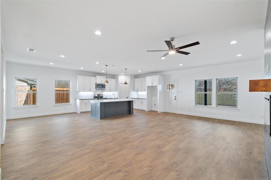 Kitchen with ceiling fan, pendant lighting, a center island with sink, white cabinets, and appliances with stainless steel finishes