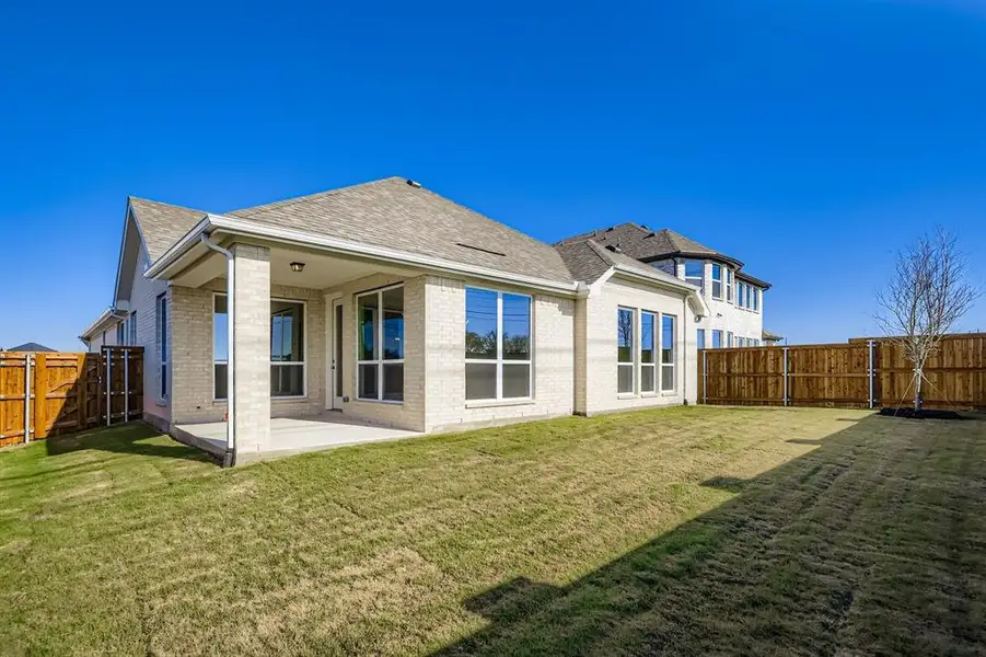Rear view of property with a shingled roof, a patio, brick siding, and a fenced backyard