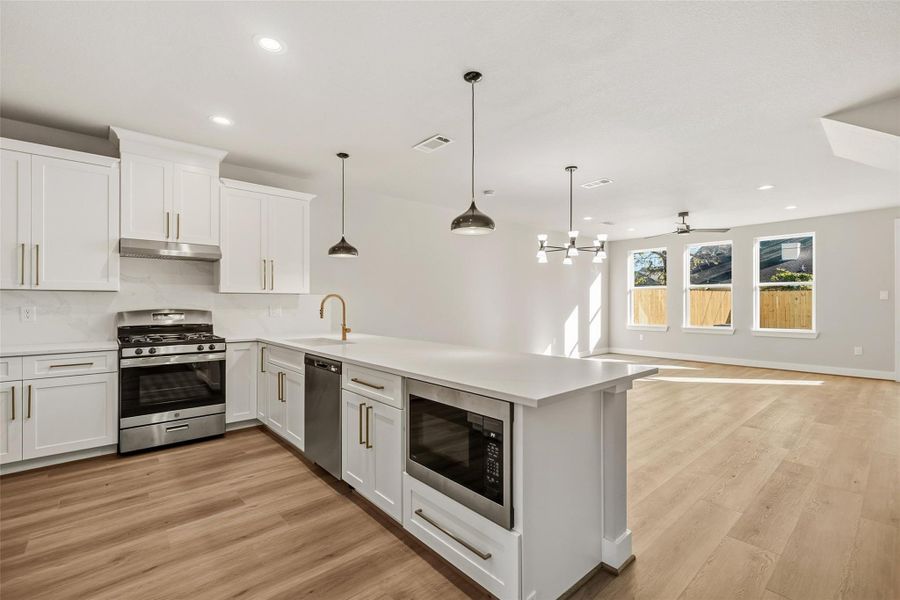 This photo showcases a spacious, modern open-concept kitchen and living area. The kitchen features sleek white cabinetry, stainless steel appliances, and a large island with pendant lighting. The living area has ample natural light from large windows and beautiful wood flooring, creating a warm, inviting atmosphere.