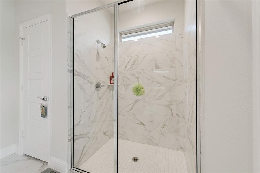 Primary bath with a marble finish shower and marble finish flooring Primary bath with a marble finish shower and marble finish flooring