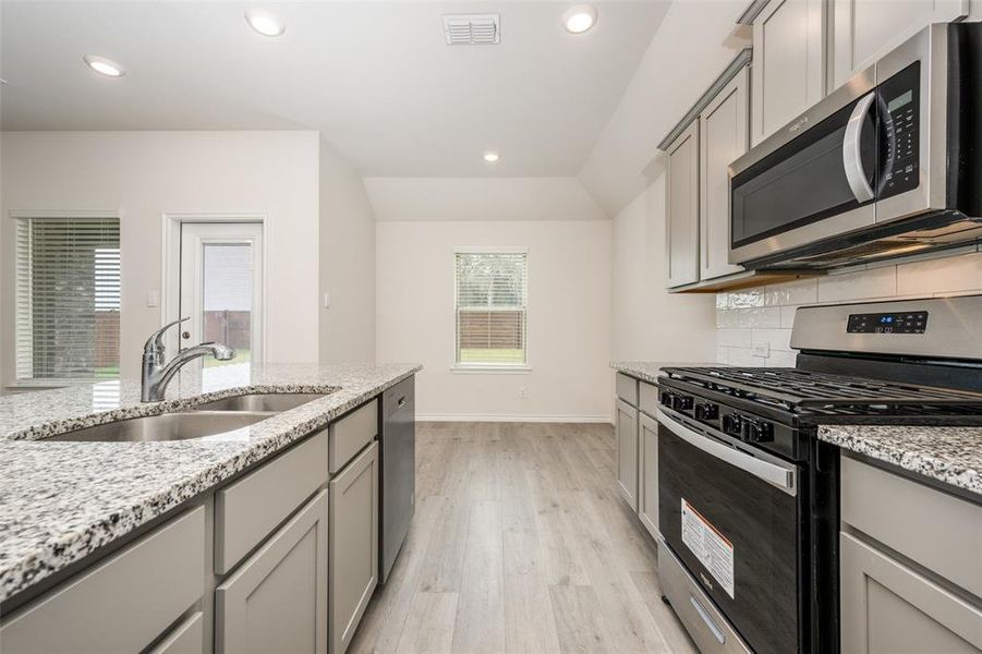 Kitchen featuring stainless steel appliances, gray cabinets, recessed lighting, light stone countertops, and light wood-style floors