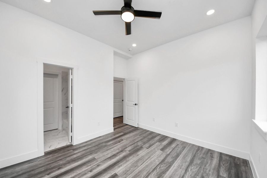 This photo features a bright, modern room with white walls and vinyl flooring. It has a ceiling fan with recessed lighting and access to a bathroom and another room through white doors. Ideal for a clean, minimalist aesthetic. This photo features a bright, modern room with white walls and vinyl flooring. It has a ceiling fan with recessed lighting and access to a bathroom and another room through white doors. Ideal for a clean, minimalist aesthetic.