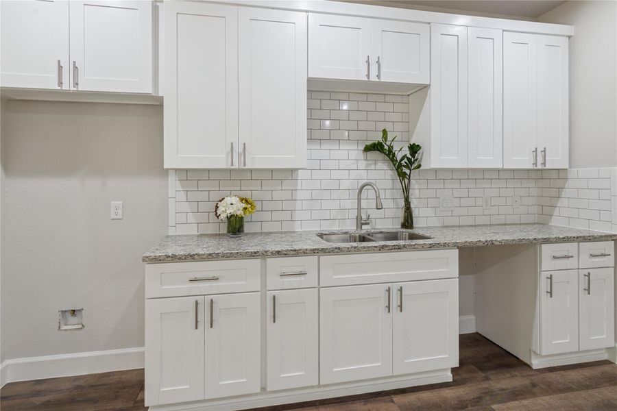 The kitchen also features sleek white, soft-closing cabinetry, a modern subway tile backsplash, and a granite countertop. The space is accented with stylish fixtures and a dual sink, offering both functionality and elegance.
