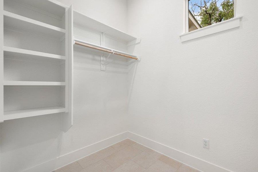 This space features built-in white shelving, a clothing rod, and a window providing natural light